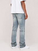 A person shown from the back wearing light-wash blue denim jeans with a white t-shirt and white sneakers, photographed against a plain light beige studio background.