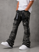 A child wearing distressed black denim flare jeans with silver paint splatter details, a black cargo pocket with 'STAKED' branding, and a white t-shirt and white sneakers, standing against a gray concrete wall.