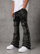 A child wearing black heavily embellished flare jeans with silver rhinestone splatter details, a white t-shirt, and white sneakers, standing against a gray concrete wall.