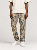 A person wearing beige camouflage pants with a white t-shirt and white sneakers, standing against a light gray studio background.
