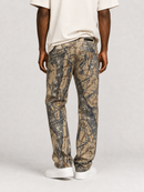 A person shown from the back wearing camouflage pants in tan, brown, and gray tones, with a cream T-shirt and white sneakers, against a light gray studio background.