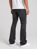 Rear view of a person wearing dark charcoal gray flared jeans, a white t-shirt, and white sneakers against a light gray studio background.